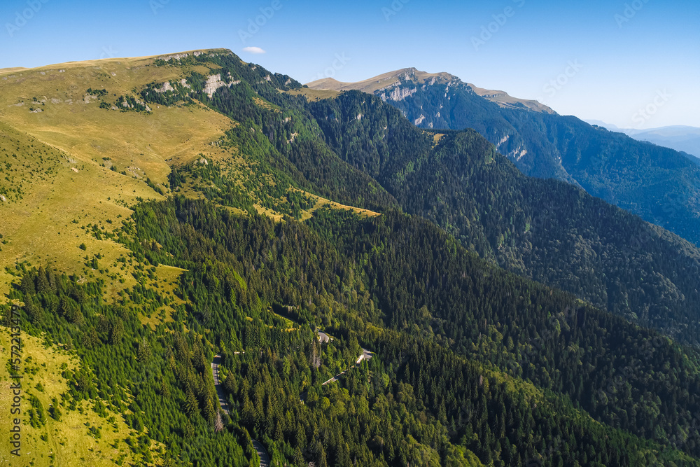 Aerial view of Bucegi Mountains and Transbucegi waving road on top of them. Landmarks of Romania, beautiful sunny summer day.