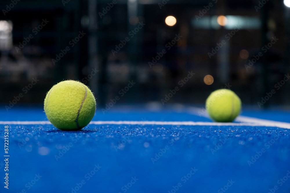 two balls on the surface of a blue paddle tennis court at night
