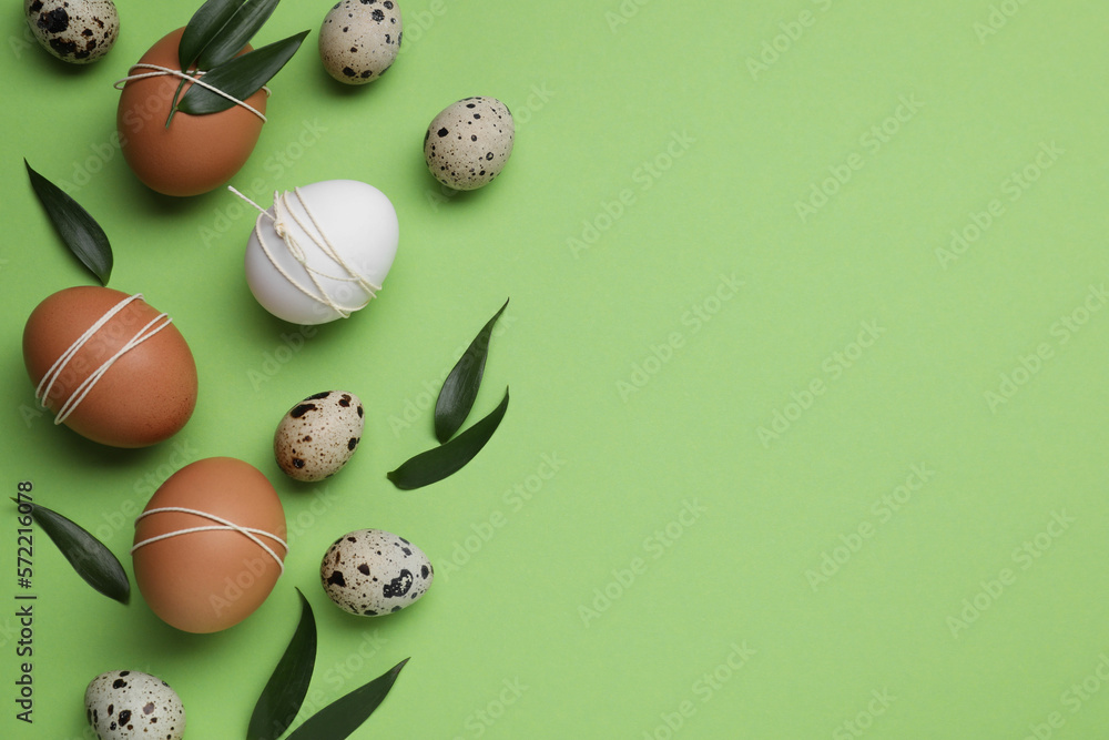 Beautifully decorated Easter eggs and leaves on light green background, flat lay. Space for text