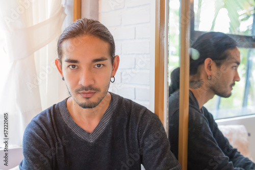 Portrait of a handsome Asian man With long hair, tied my hair to the camera, with the light shining from the back, showing a smooth expression with his reflective mirror on the side