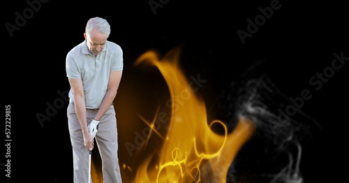 Caucasian senior male golf player holding club against fire flame effect on black background