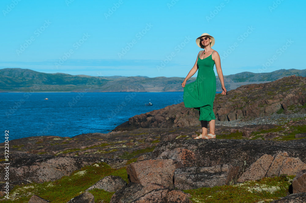 Woman tourist in a straw hat and a green dress on the seashore on a bright sunny day