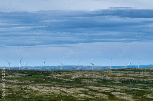 Wind farm in hilly area under cloudy sky