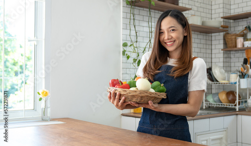 Panoramic shot of Asian woman in healthy apron preparing and holding chilli vegetables In the kitchen at home before cooking online smiling happily at the camera to stay healthy safe from disease.