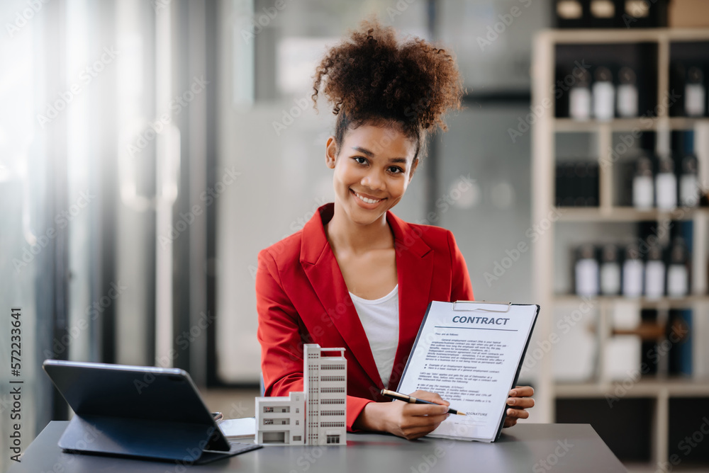 Young real estate agent worker working with laptop and tablet at table in office and small house beside it.. Young real estate agent worker working with laptop and tablet at table in office and small house beside it..