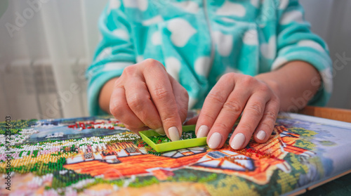 The hands of a woman embroidering a picture with beads. Close-up view. DIY. SDOF.