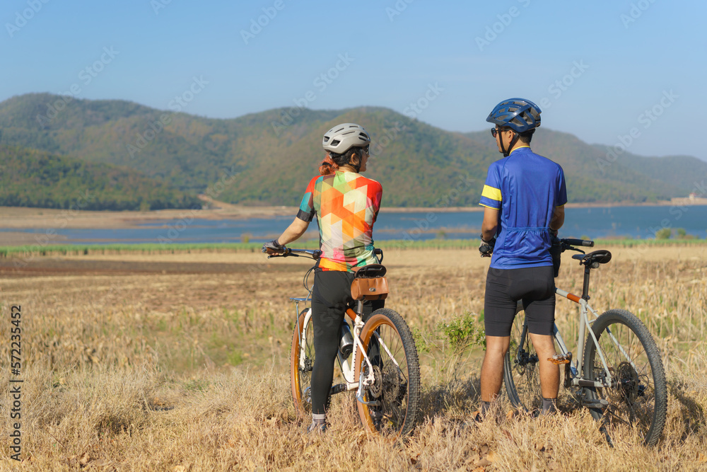 Asian cyclist couple looking at lake and mountain view and chatting while taking a break from the morning bike ride