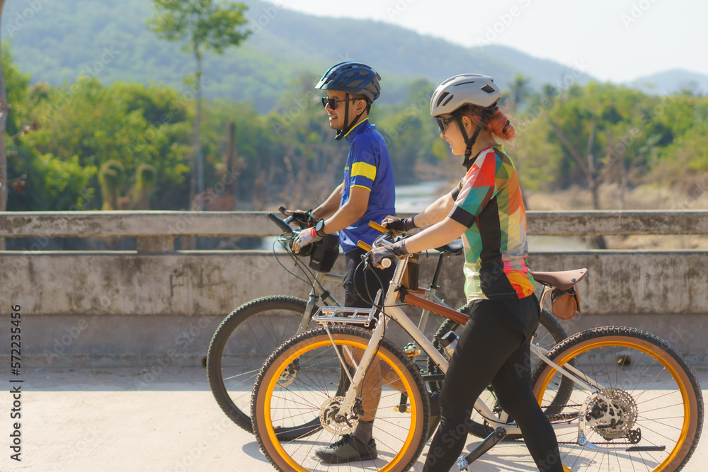 Asian cyclist couple taking a break from cycling take a break to walk and walk and talk to each other to relax.