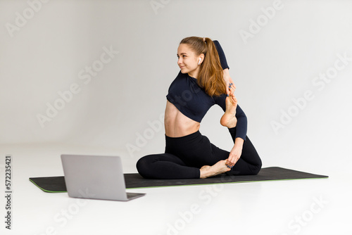 Remote fitness lesson, young woman doing stretching with laptop.