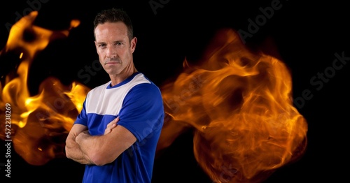 Composition of male basketball player with arms crossed over flames on black background