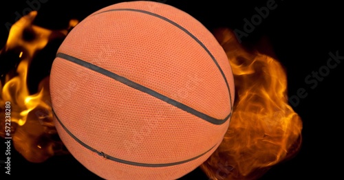 Composition of basketball ball surrounded by flames on black background