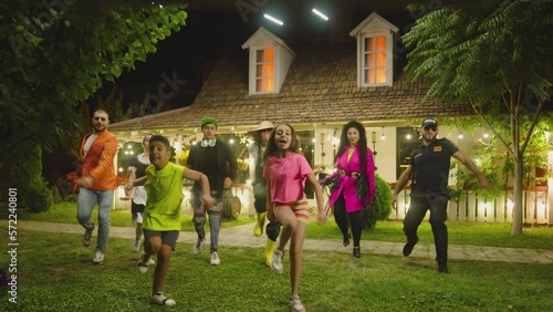 Group of funny , stylish  multi aged dancers dancing near village house at night . Kids dancing with house workers . Multi ethnic people having fun . Beautiful background with different lights .