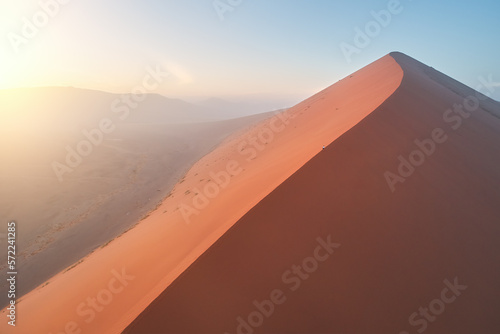 A lonely man climbing to the top of huge orange sand dune in early morning: feeling of sunrise over ancient Namib desert. Namib-Naukluft National Park, Namibia. © Martin Mecnarowski