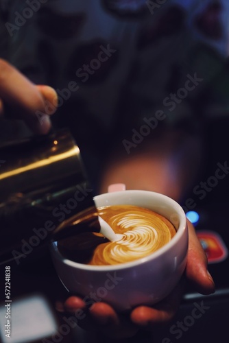 Close up barista hands making coffee latte art over dark background.