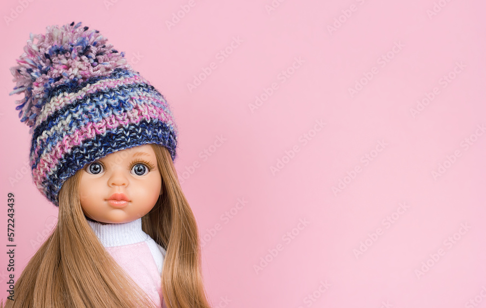Doll with beautiful blond hair and a cute face in a knitted hat close-up portrait, sale of children's toys and knitted clothes, selective focus