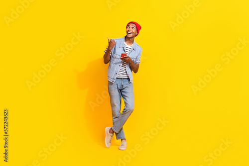 Full length photo of positive excited man wear jeans outfit typing modern gadget thumb empty space isolated yellow color background
