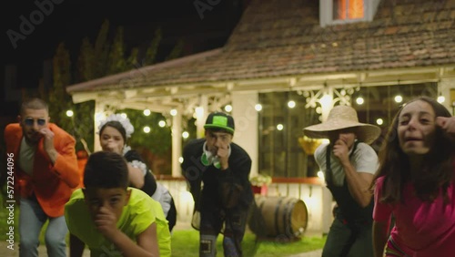 Group of funny , stylish  multi aged dancers dancing near village house at night . Kids dancing with house workers . Multi ethnic people having fun . Beautiful background with different lights .