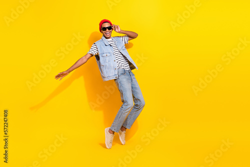 Full length photo of cute cheerful guy dressed denim clothes dark eyewear having fun empty space isolated yellow color background