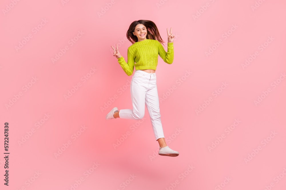 Full length photo of cute young girl jumping show double v-sign active wear trendy green outfit isolated on pink color background Full length photo of cute young girl jumping show double v-sign active wear trendy green outfit isolated on pink color background