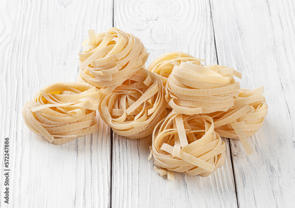 Uncooked tagliatelle pasta on white wooden backgrond