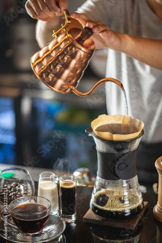 drip coffee, Barista making drip coffee by pouring spills hot water on coffee ground with prepare filter from copper pot to glass transparent chrome drip maker on wooden table in cafe shop