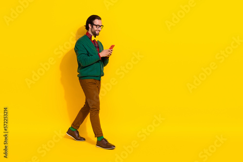 Full size profile photo of positive person walk use telephone empty space isolated on yellow color background