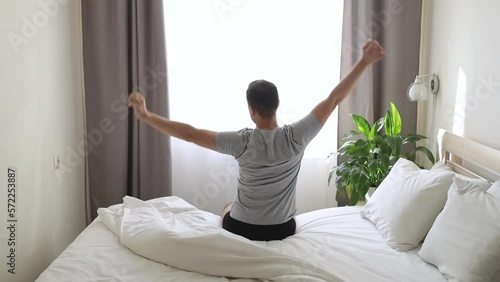 The man woke up in the morning and stretched in bed looking out the window.