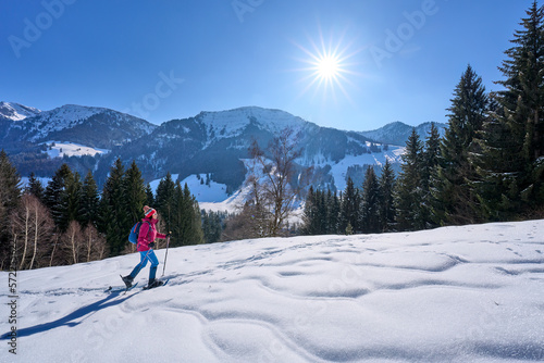 nice and active senior woman snowshoeing in deep powder snow below Mount Hochgrat in the mountains of the Allgau alps near Oberstaufen and Steibis, Bavaria, Germany