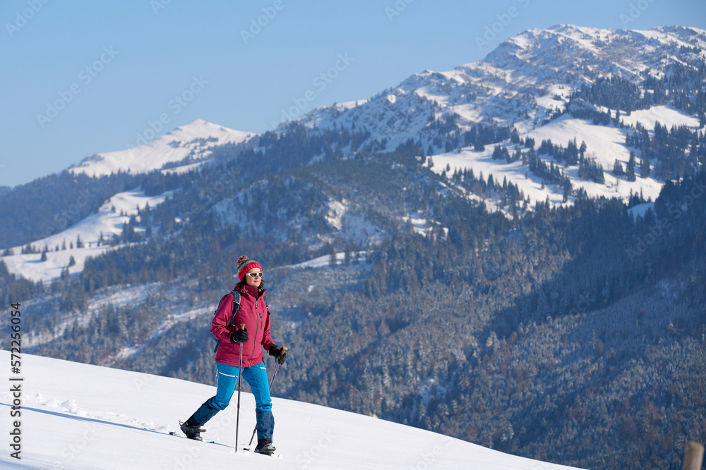 nice and active senior woman snowshoeing in deep powder snow below Mount Hochgrat in the mountains of the Allgau alps near Oberstaufen and Steibis, Bavaria, Germany