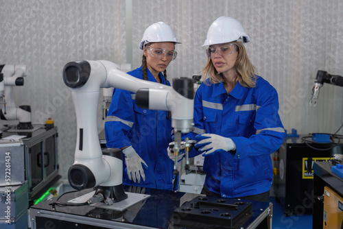 Female senior robotic engineer in modern factory teach new comer operate and maintenance robot arm