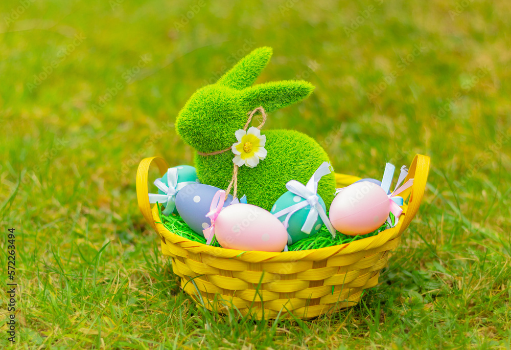 Fototapeta premium green grass rabbit in basket with colorful eggs on the meadow. Easter symbol, decor, bunny figure