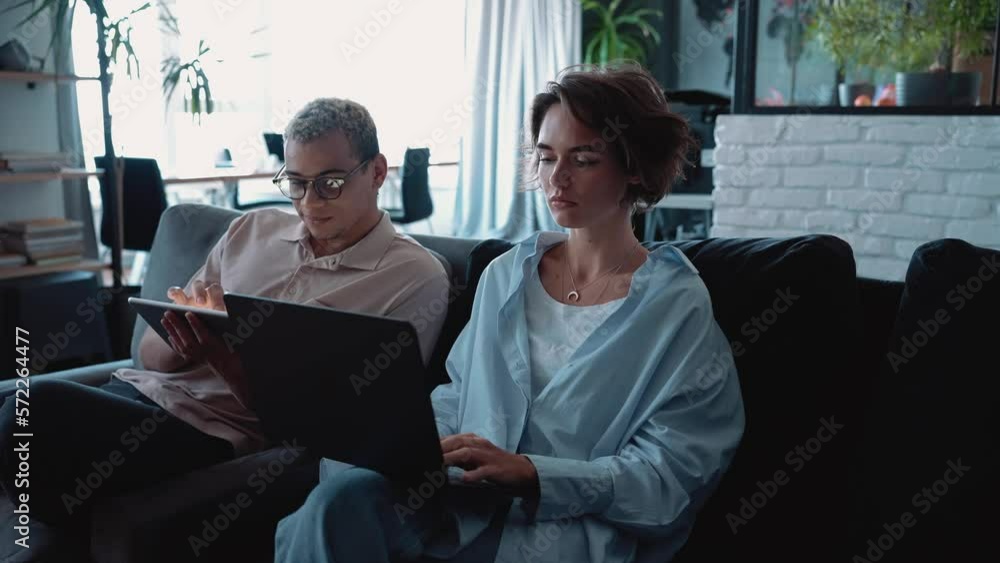 Smiling man with piercing and dyed blond hair working on tablet and talking with brunette woman in the office Smiling man with piercing and dyed blond hair working on tablet and talking with brunette woman in the office