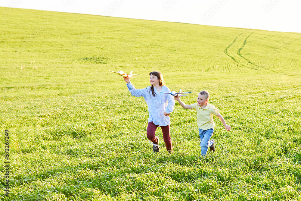 Cheerful and happy children play in the field and imagine themselves to be pilots on a sunny summer day. Kids dreams of flying and aviation.