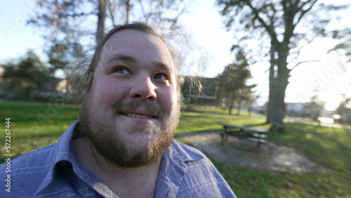 One happy chubby young man standing outdoors at park enjoying nature. Male caucasian person in contemplation