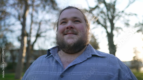 Joyful young man walking outside at park in slow motion. Portrait of a happy overweight 20s guy walks outdoors in nature