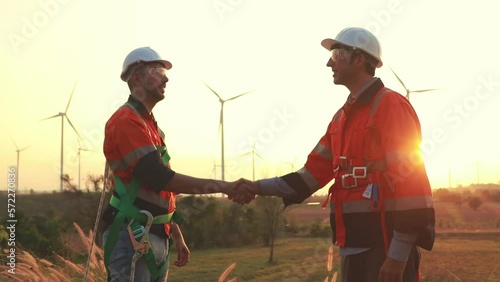 Two male technicians shake hands as the wind turbine maintenance work succeeds at sunset before departing for home.