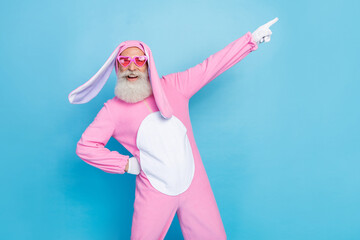 Photo of funky positive man dressed pink rabbit costume sunglass directing empty space hand on waist isolated on blue color background