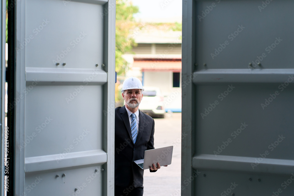 A Foreman in black suit and white safety helmet use laptop and check product in container box after open door A Foreman in black suit and white safety helmet use laptop and check product in container box after open door