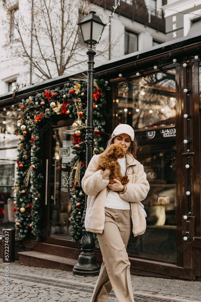 Young woman holding a puppy, walking on christmas city background