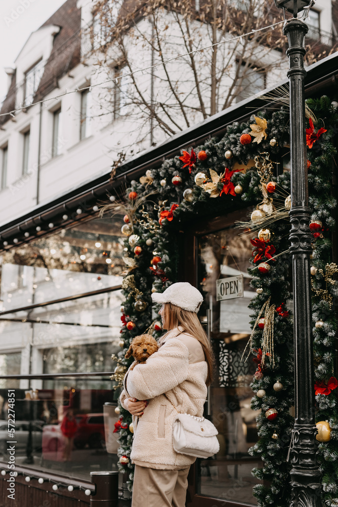 Young woman holding a puppy, walking on christmas city background
