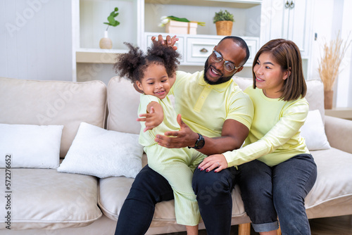 Young family with small daughter sitting on sofa playing and laughing together in the living room