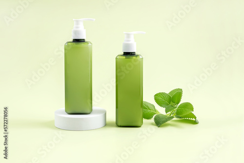 bottle for cosmetics on a white podium and mint leaves on a light green background