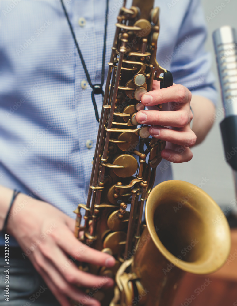Obraz premium View of a saxophone player in headphones during rehearsal, recording sound for new album song at studio, saxophonist musician in front of microphone with musical band orchestra, music production