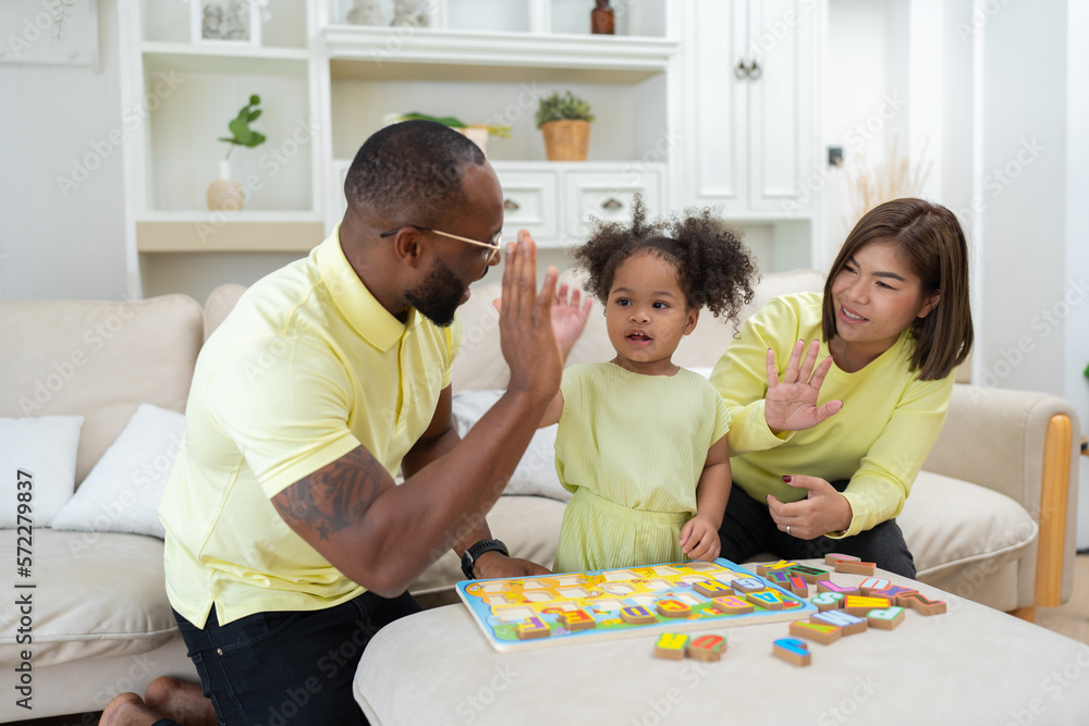 Young family with small daughter sitting on sofa playing arrange alphabet in the living room Young family with small daughter sitting on sofa playing arrange alphabet in the living room