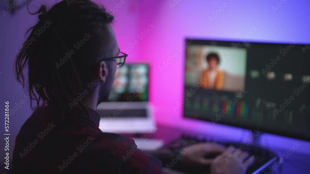 Young man in glasses working on video editing on computer doing montage and color correction. Professional man hand making edits on a special panel. Concept of creating video content. Young man in glasses working on video editing on computer doing montage and color correction. Professional man hand making edits on a special panel. Concept of creating video content.
