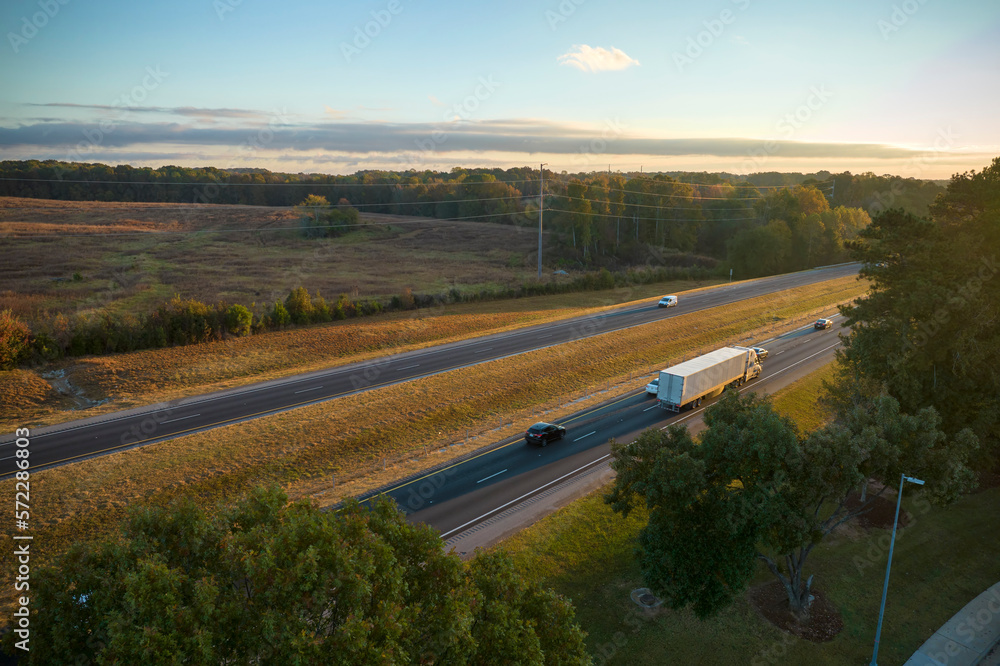 View from above of busy american highway with fast moving traffic between autumn woods. Interstate transportation concept