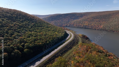 Mountains in Fall season colors with cars traveling on highway beside peaceful river