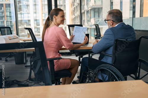 Businessman in wheelchair and friendly company employee adjust working papers