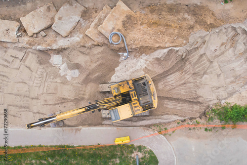 Yellow heavy excavator excavating sand and working during road works, unloading sand during construction of the new road, aerial drone top view