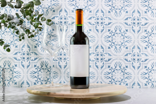 Mockup of bottle of red wine. Bottle with red wine on wooden podium opposite tile wall with eucalyptus leaves and shadows. Presentation, advertising or promotion sale natural wine. Front view